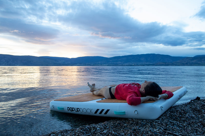 Women lays ontop of a PopBoard Inflatable Dock Platform near the waters edge.