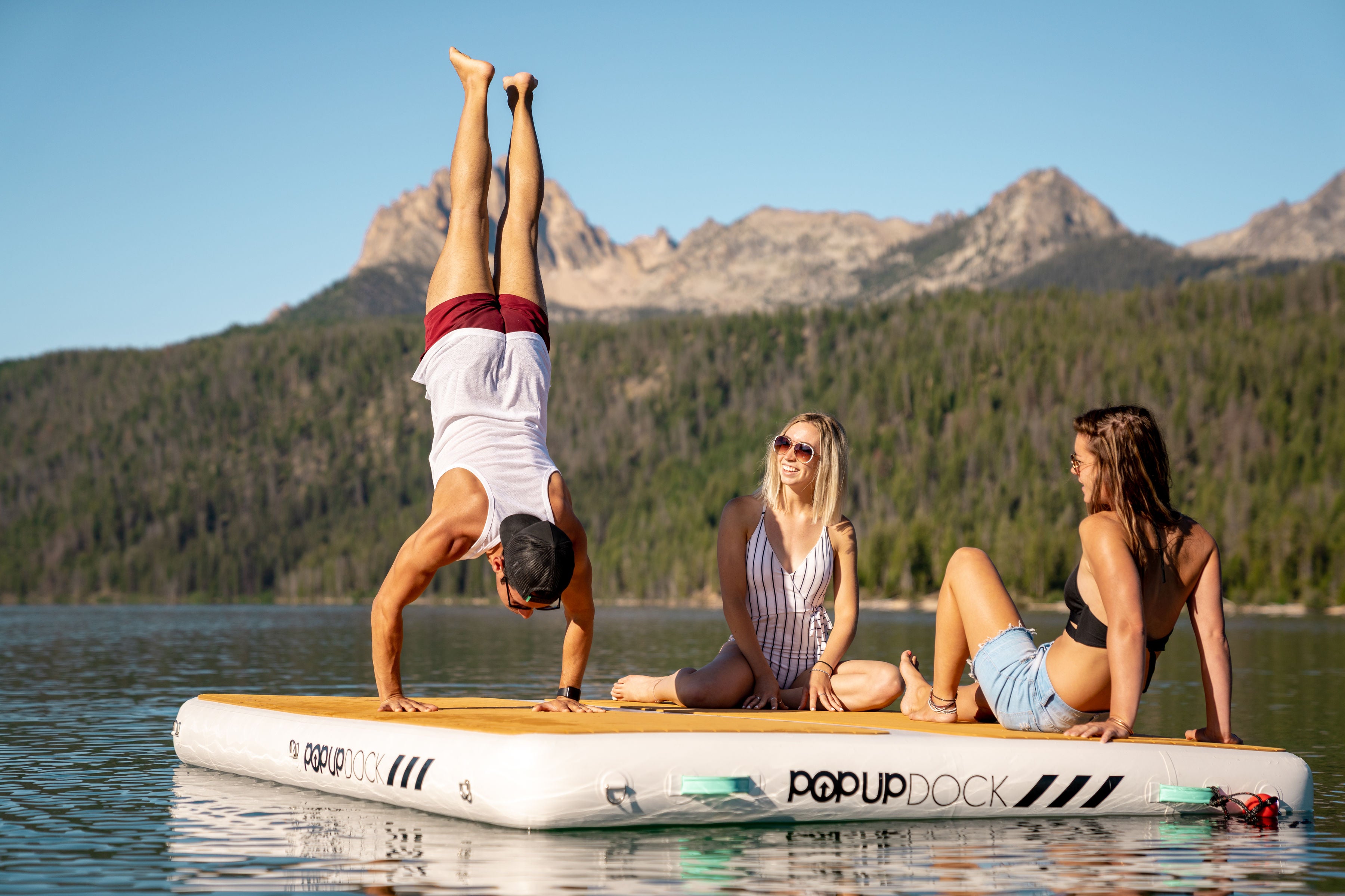 Man does a handstand in front of friends all ontop of a PopBoard PopUp Inflatable dock platform floating on the water.