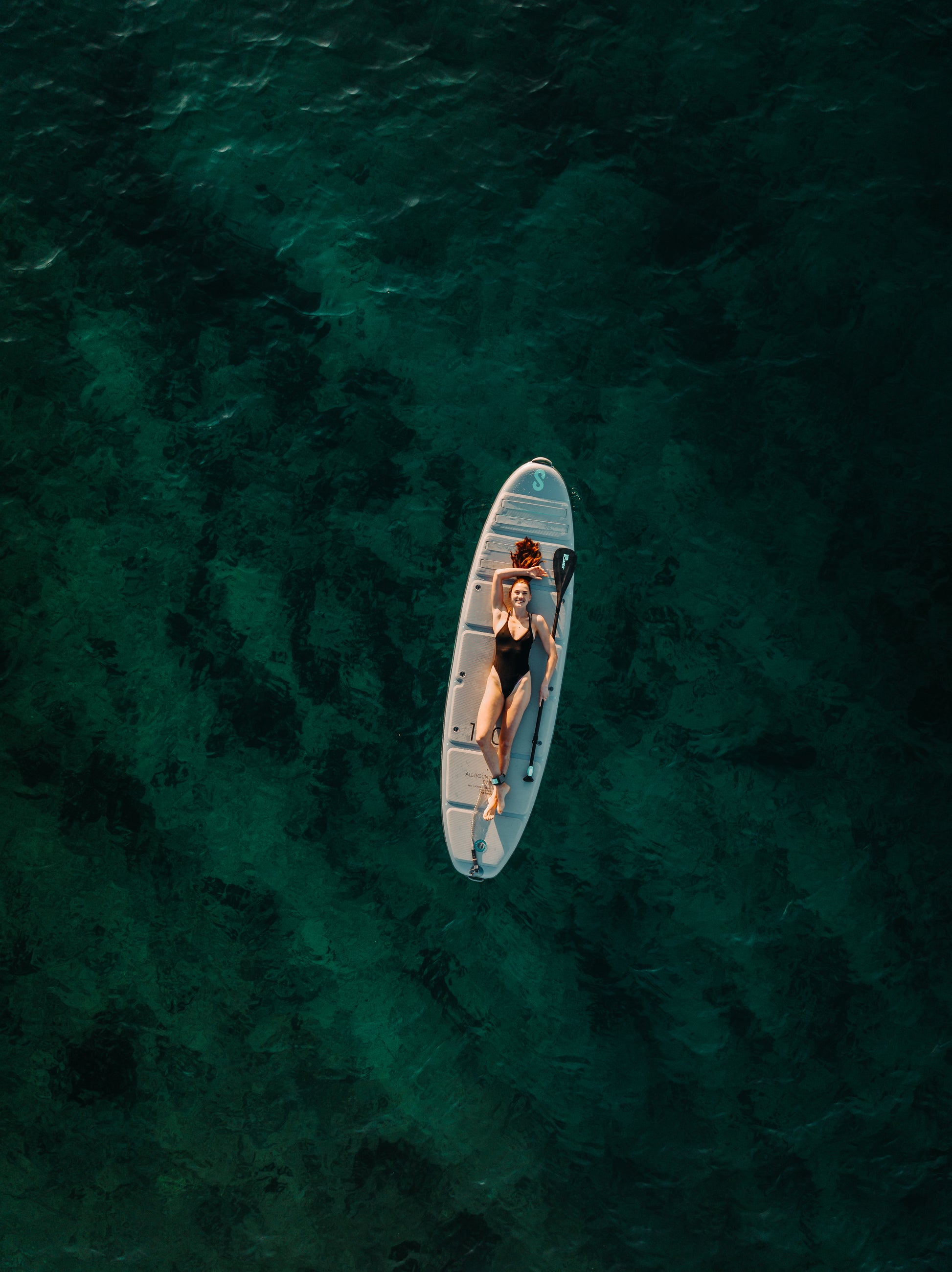 Woman laying down floating on SIPA Boards Alpha One Electric Paddleboard with self-inflating design and assist power unit floating on the water with sailboats. Ships free from e-boarders.com.