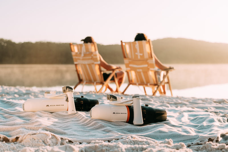 Vacationers sitting on beach with Aqua Marina BLUEDRIVE X Pro electric-assist fin system. Includes wireless remote control and rechargeable battery. Designed for paddleboarders, snorkelers, and recreational swimming. Free shipping at e-boarders.com