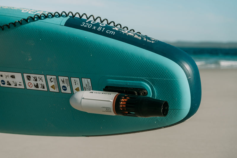 Attached and mounted to a paddleboard middle fin adaptor is the Aqua Marina BLUEDRIVE X Pro electric-assist fin for paddleboards and kayaks with rechargeable battery and wireless remote control. Free shipping at e-boarders.com