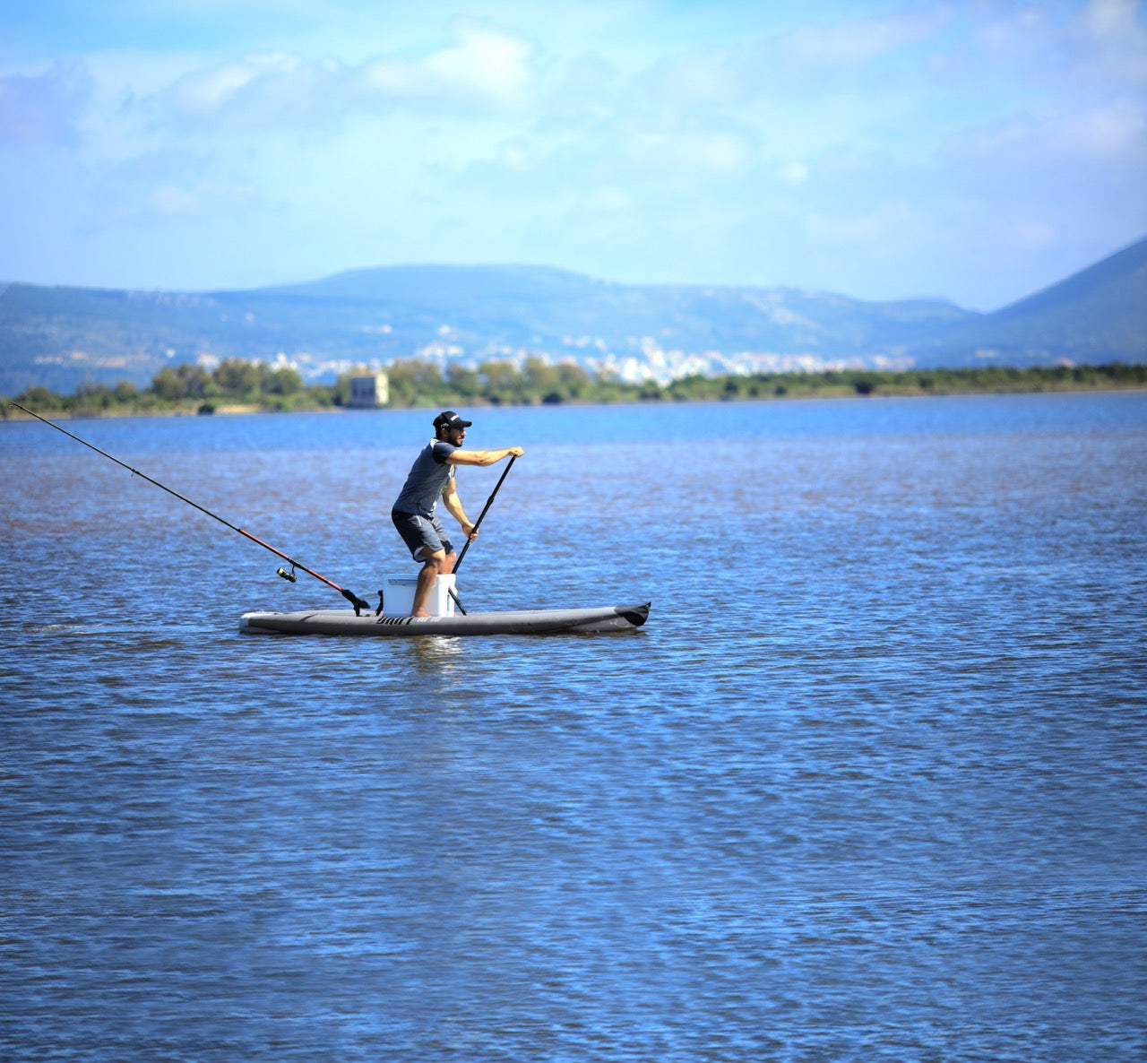 Lifestyle photo man paddling to cast a fishing rod line on Aqua Marina Drift iSUP with rod holder — ships free at e-boarders.com