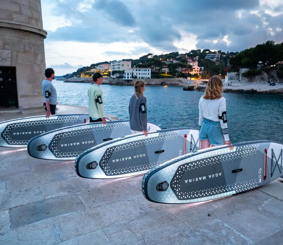 Aqua Marina Glow Paddleboard illuminating with four people and four boards on a pier ready to paddle. Buy at E-Boarders.com