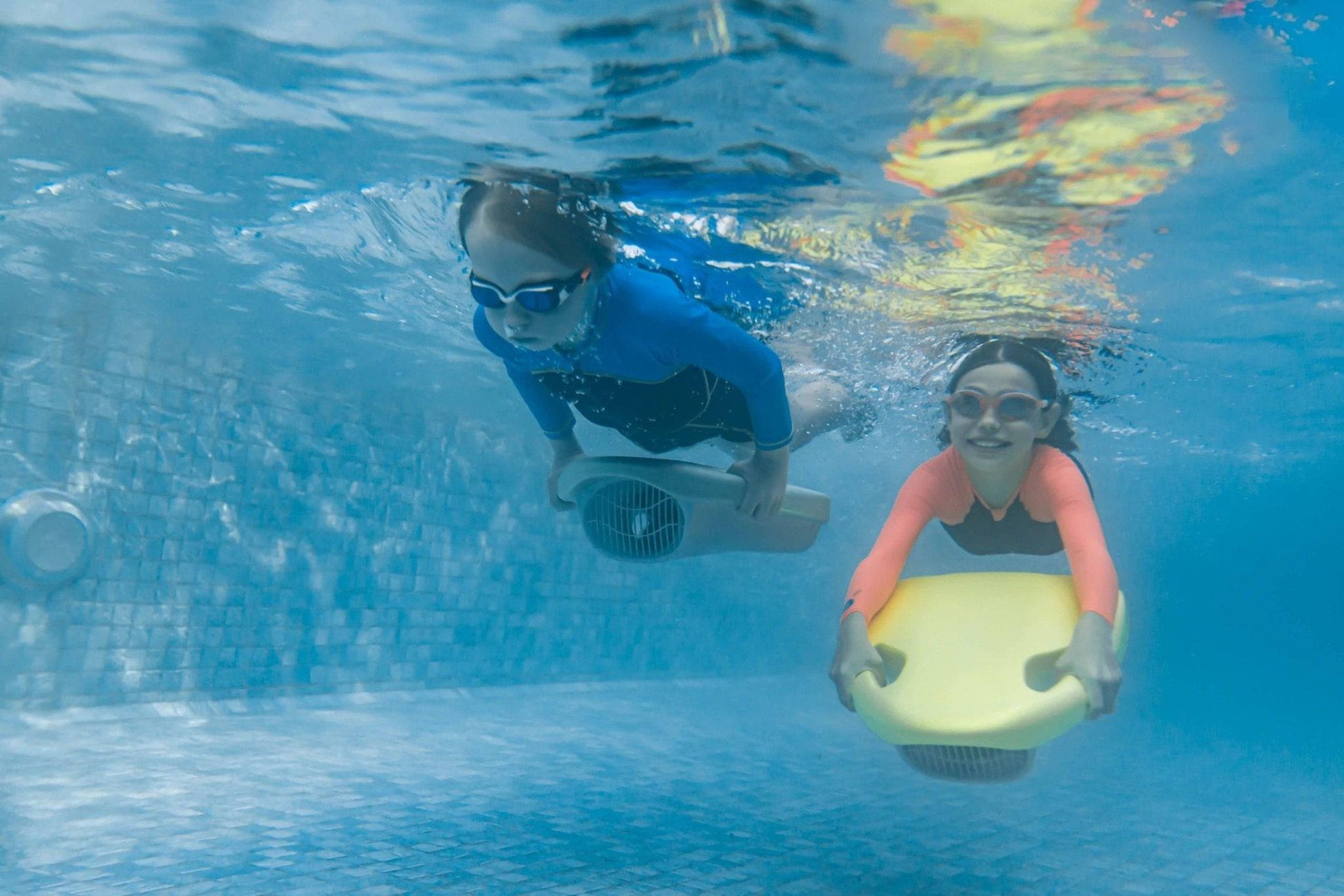 Two pool swimmers with ASIWO MAKO electric swimming kickboard in yellow and blue for aquatic swim assistance. Ships free at e-boarders.com