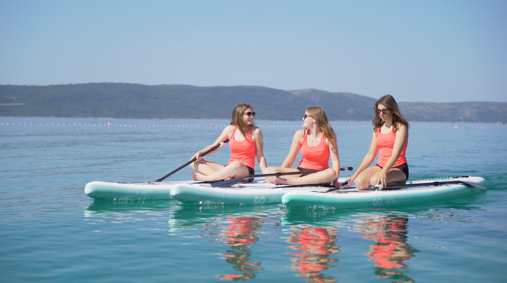 Three female paddlers sitting on three SIPA Boards Alpha One Electric Paddleboard with self-inflating design and assist power unit floating on the water with sailboats. Ships free from e-boarders.com.