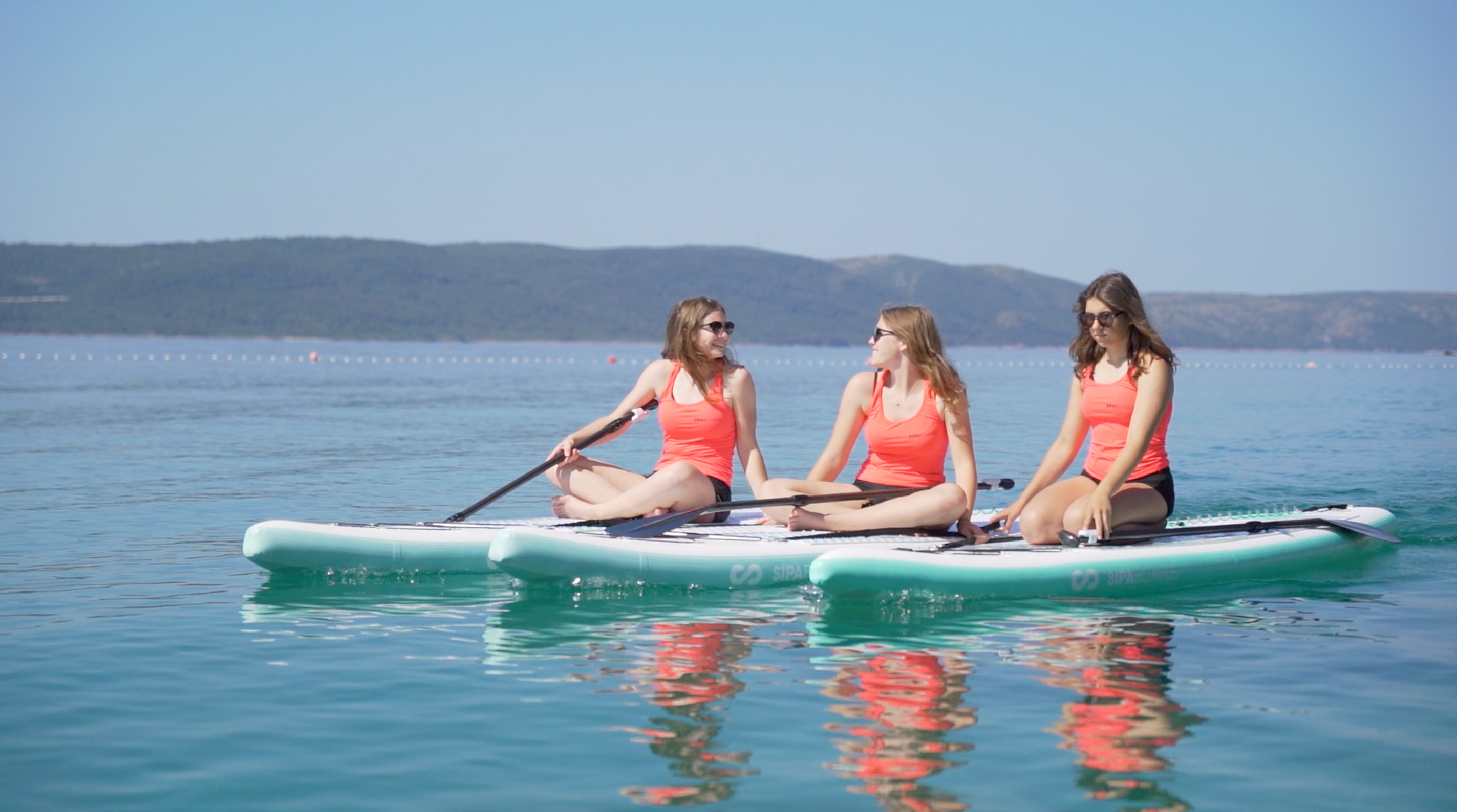Three female paddlers sitting on three SIPA Boards Alpha One Electric Paddleboard with self-inflating design and assist power unit floating on the water with sailboats. Ships free from e-boarders.com.
