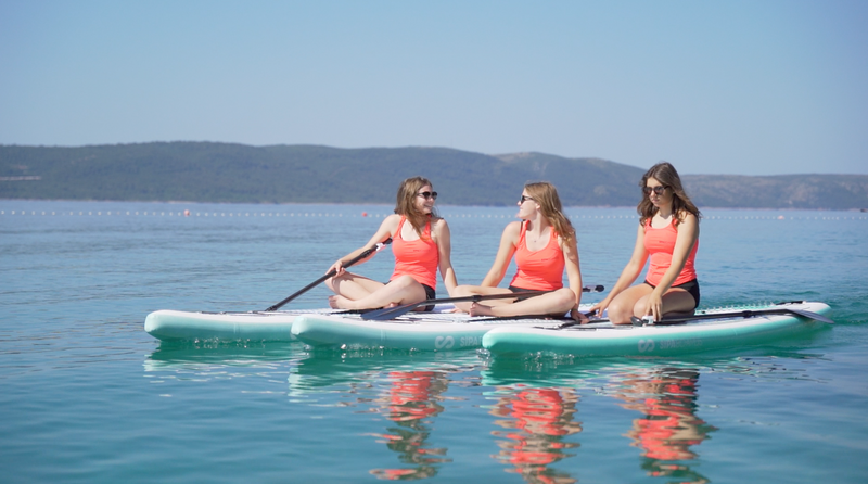 Three female paddlers sitting on three SIPA Boards Alpha One Electric Paddleboard with self-inflating design and assist power unit floating on the water with sailboats. Ships free from e-boarders.com.