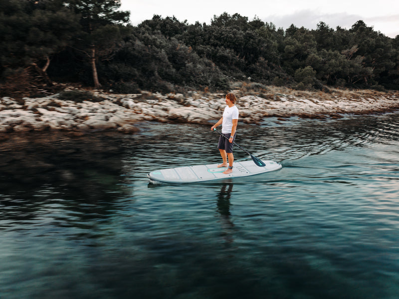 Man paddling on SIPA Boards Alpha One Electric Paddleboard with self-inflating design and assist power unit floating on the water with sailboats. Ships free from e-boarders.com.