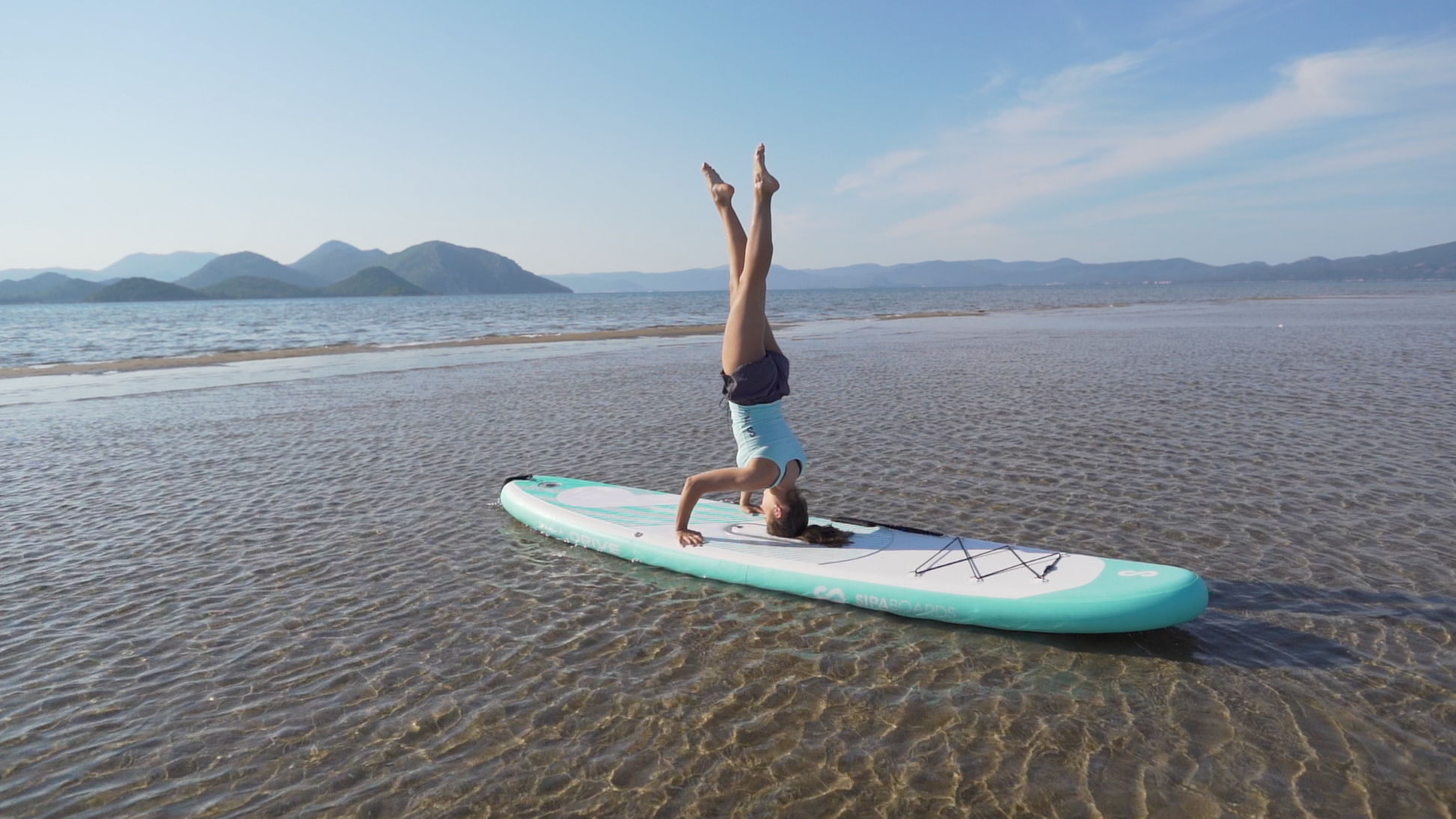 Female performing headstand on a SIPA Boards Alpha One Electric Paddleboard with self-inflating design and assist power unit floating on the water with sailboats. Ships free from e-boarders.com