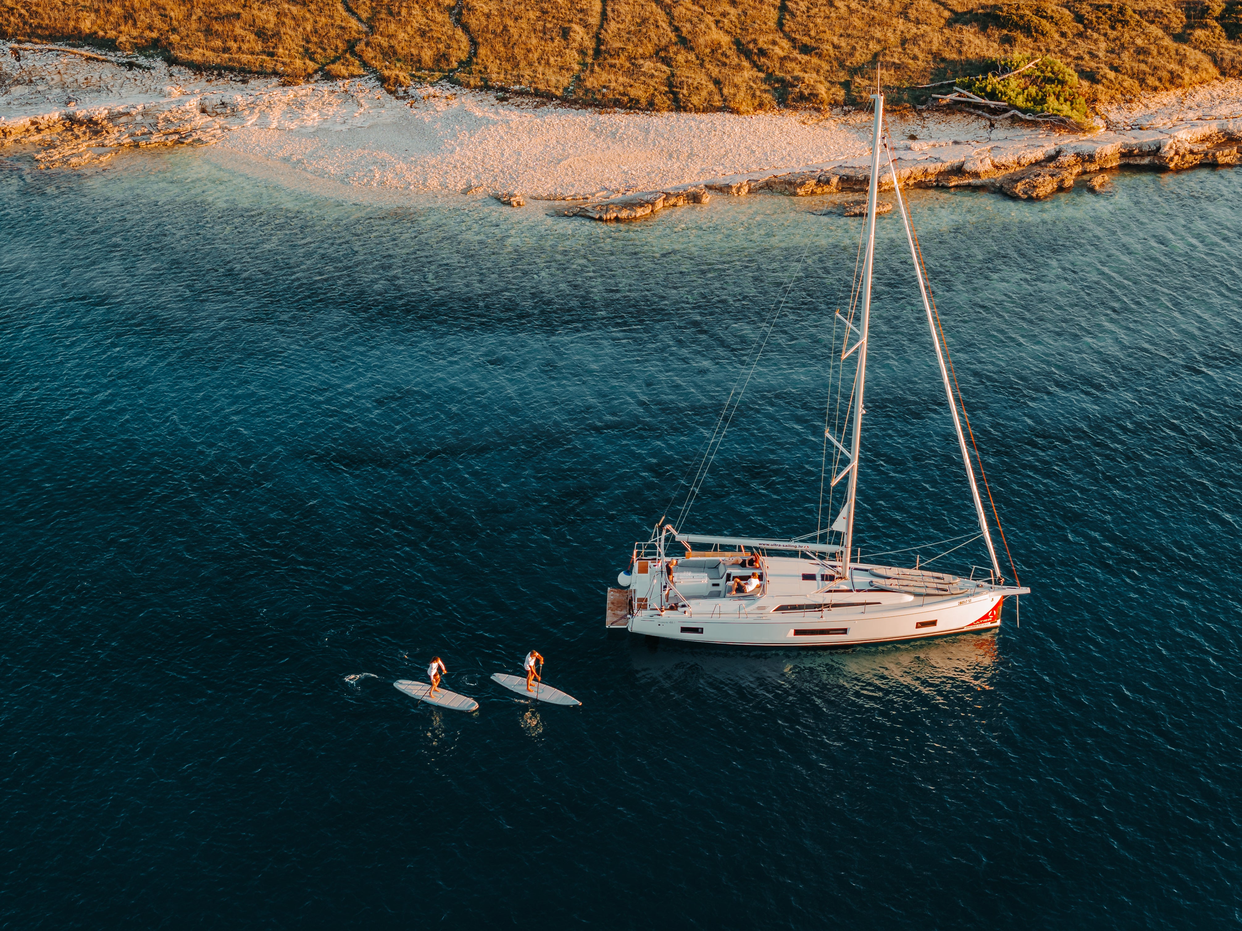 Two paddlers near sailboat on SIPA Boards Alpha One Electric Paddleboard with self-inflating design and assist power unit floating on the water with sailboats. Ships free from e-boarders.com.