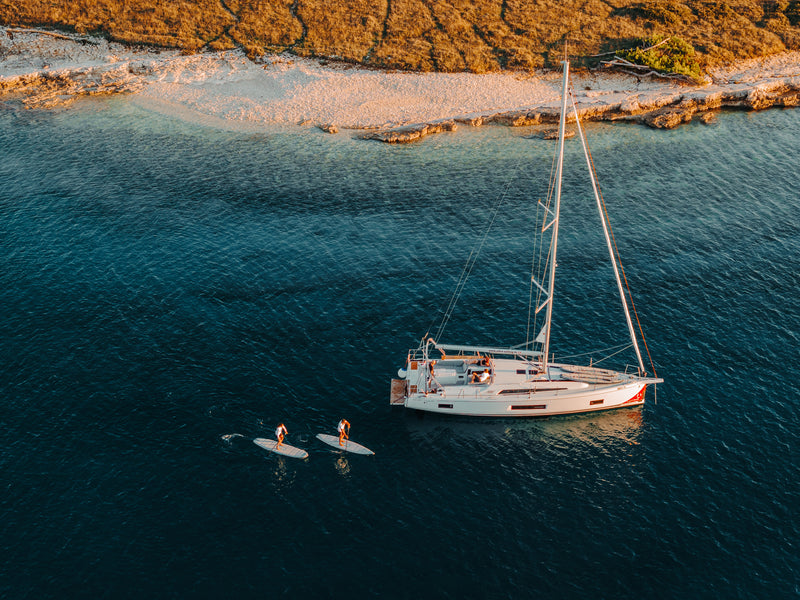 Two paddlers near sailboat on SIPA Boards Alpha One Electric Paddleboard with self-inflating design and assist power unit floating on the water with sailboats. Ships free from e-boarders.com.