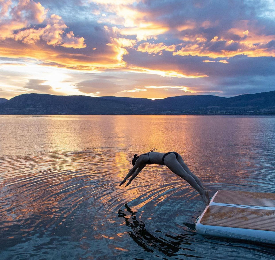 Woman dives off of a PopBoard Inflatable Dock Platform into the water at sunset.